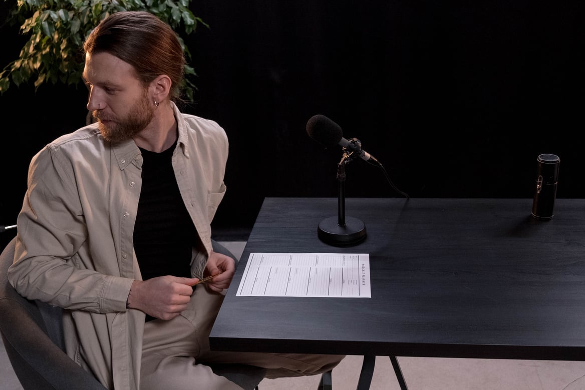 A Man in Brown Long Sleeves Sitting on a Chair Near Microphone on Wooden Table